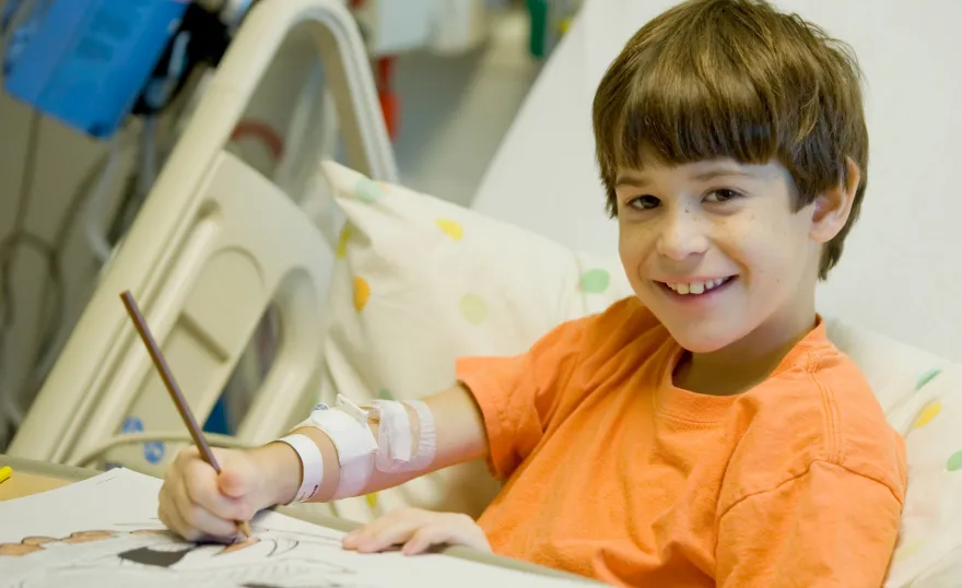 Un garçon dessine le sourire aux lèvres à son lit d'hôpital